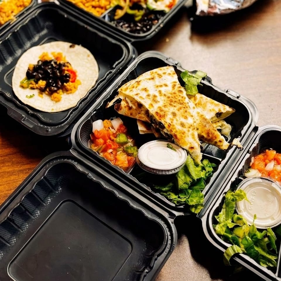 Multiple black takeout containers filled with Mexican food like quesadillas, tacos, and salsa.